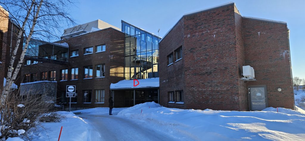 A path to a red brick building with a slanting glass roof above the entrance. The entrance is labelled "D" in the picture.
