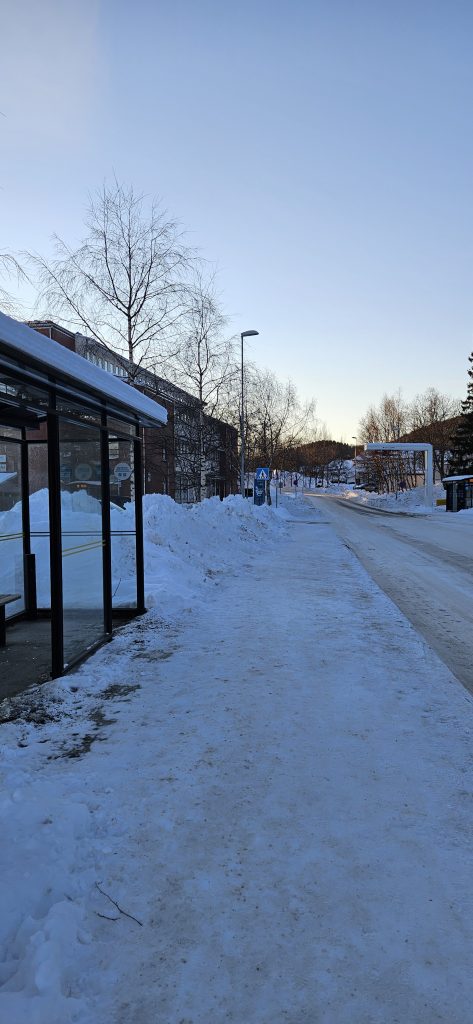 A road with a bus stop at each side and a building on its left side.